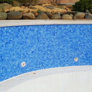 Empty swimming pool with blue mosaic tiles and stone edge.