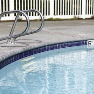 Clear blue water in a swimming pool with metal handrails by the edge.