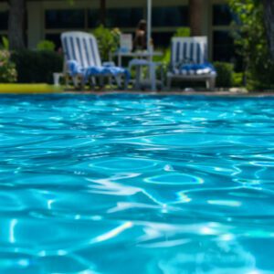 Clear blue swimming pool water with lounge chairs in the background.