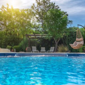 Bright sunny day at a serene backyard pool surrounded by trees and lounge chairs.