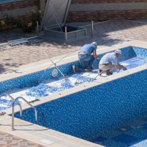 Two people working inside an empty swimming pool under renovation.