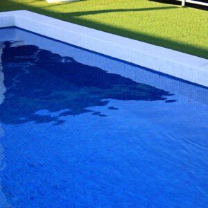 A blue swimming pool with clear water and green grass nearby.