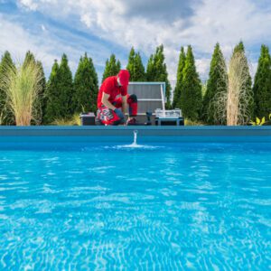 Person in red suit working near a pool with clear blue water.