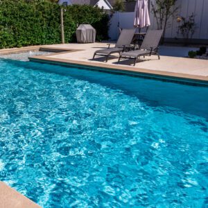 Clear blue swimming pool with two lounge chairs on the deck.