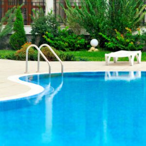 Clear blue swimming pool with a white pool ladder and greenery surrounding it.