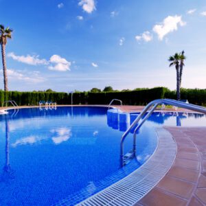 A serene outdoor pool under a bright blue sky with palm trees.