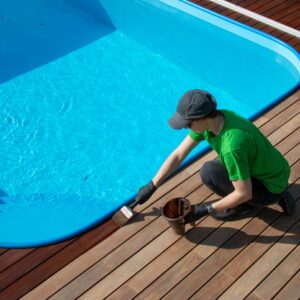 Person cleaning the edge of a swimming pool with a brush.