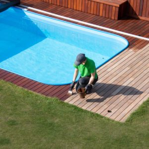 Person installing wooden decking around a pool on a sunny day.
