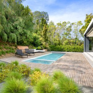 Modern backyard with a swimming pool, lounge chairs, and lush greenery.
