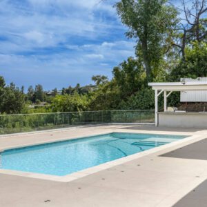 Modern outdoor pool area with clear blue water and greenery.