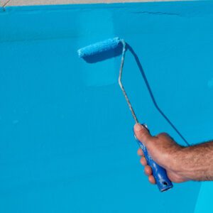 A hand painting a wall bright blue with a roller.