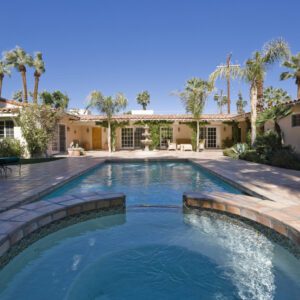 Modern house with a swimming pool and palm trees under a clear blue sky.