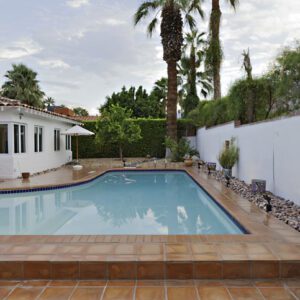 A serene backyard pool area surrounded by white walls and palm trees.