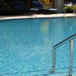 A clear, inviting swimming pool with metal handrails and lounge chairs in the background.