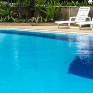 Clear blue swimming pool with white lounge chairs and greenery.