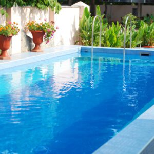 Clear blue swimming pool surrounded by plants and white walls.