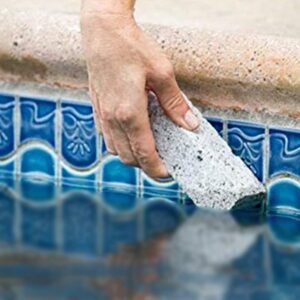 Hand cleaning pool tiles with a pumice stone.