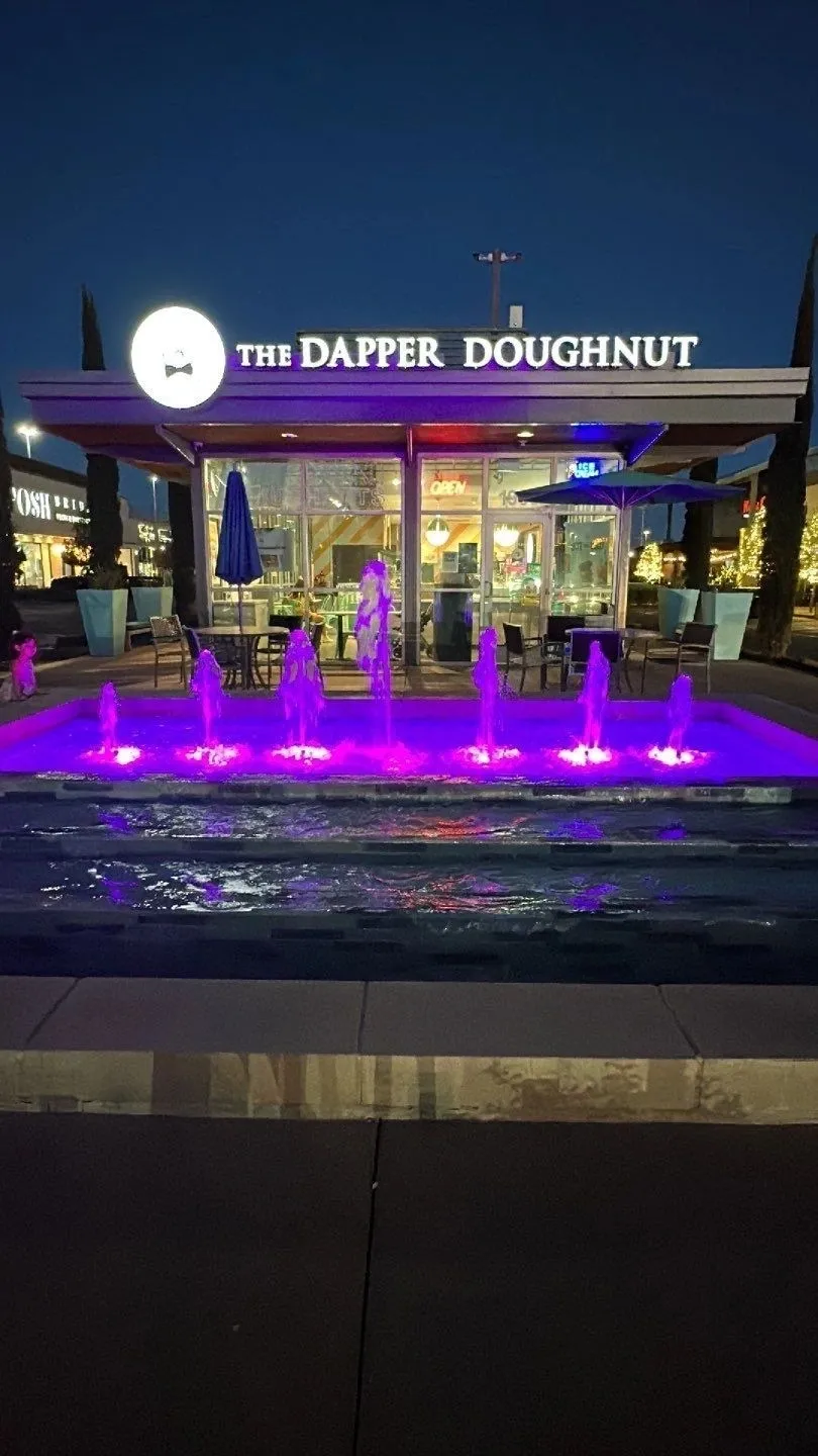 The Dapper Doughnut shop with vibrant purple-lit fountain in front.