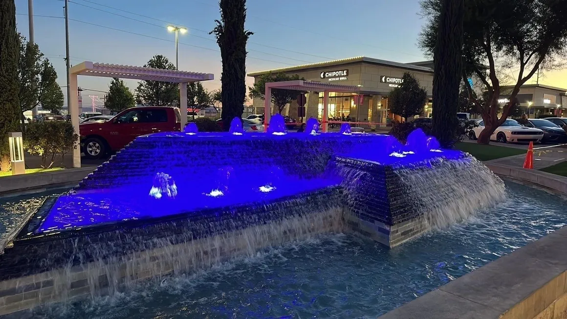 Blue-lit fountain cascading water in front of a building at dusk.
