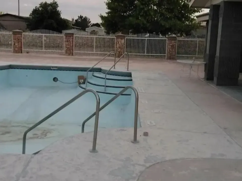 Empty outdoor swimming pool with metal handrails and concrete deck.