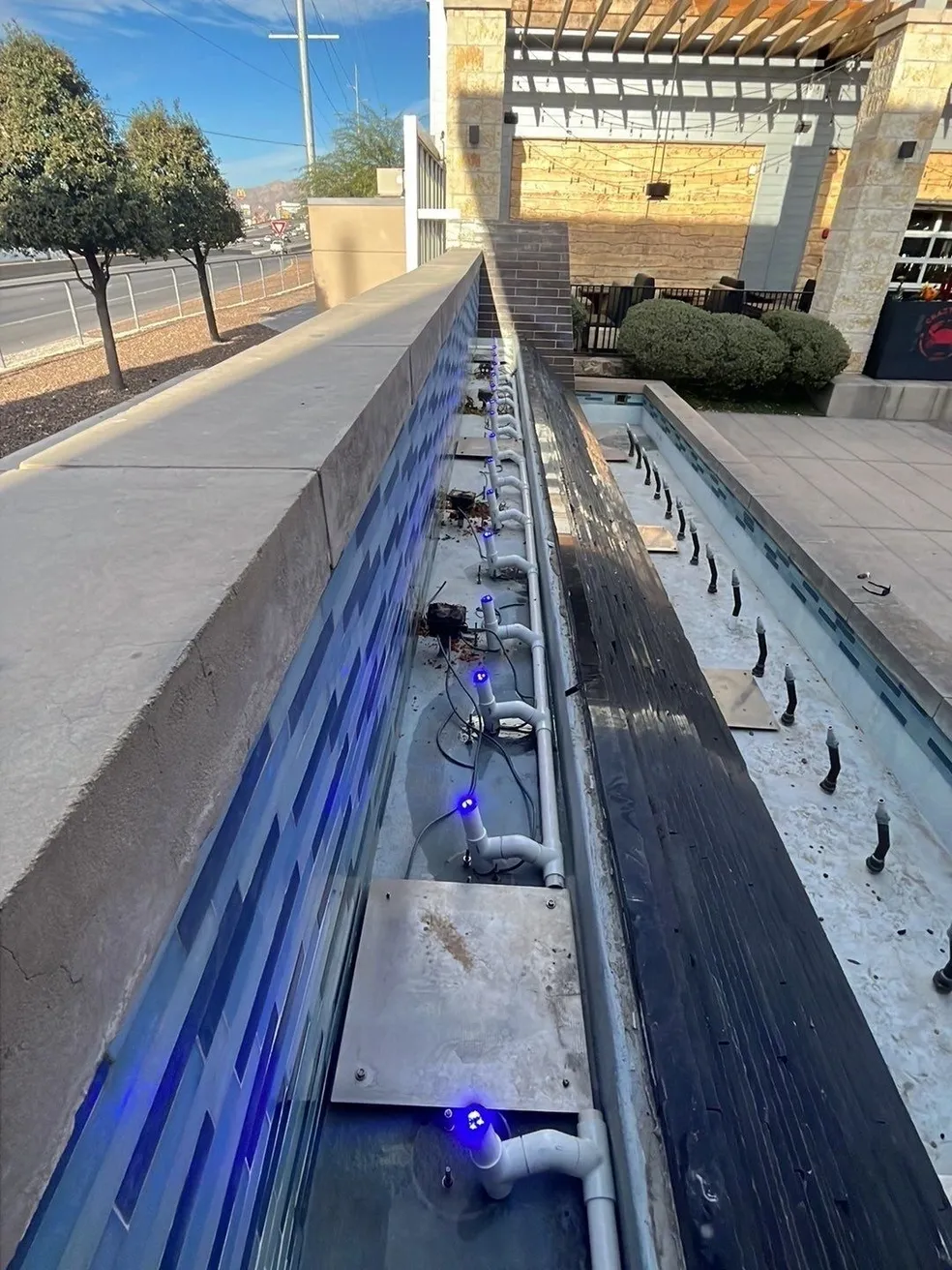 An outdoor water feature with blue lighting along a concrete structure.